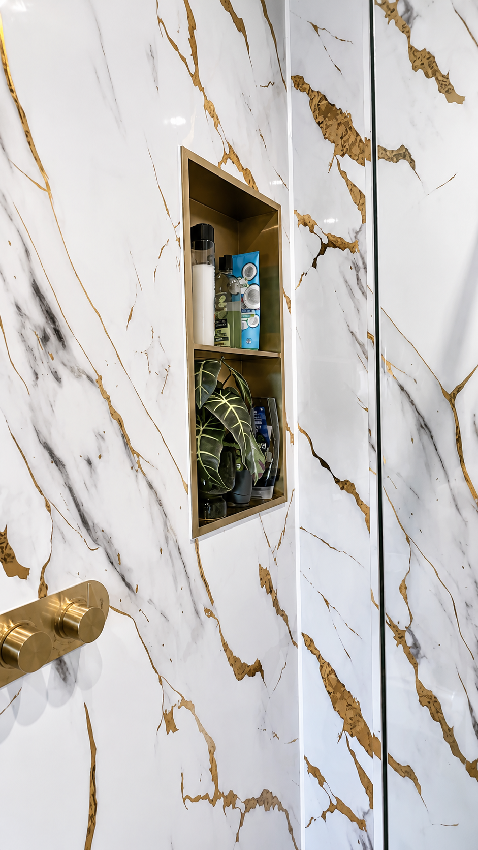 Brushed brass recessed shower niche set within marble-effect wall panels in Billericay